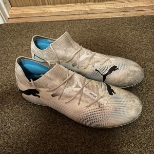 Vita Puma Future fotbollsskor - Säljer ett par vita Puma Future fotbollsskor med svart Puma-logga på sidan. Skorna har snörning och en strumpliknande ovandel i syntetmaterial för skön passform. Rund tå och platt sula, perfekt för dig som vill ha grym kontroll på planen. Inga skador på skorna bara lite smutsiga för jag har spelat på konstgräs därför säljs dom till ett sånt bra pris 