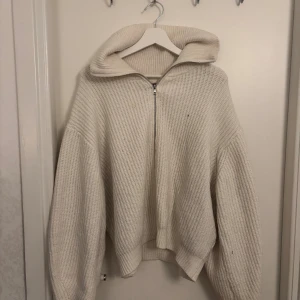 Vit stickad tröja med dragkedja - Säljer en oversized vit stickad tröja med stor krage och dragkedja framtill. Tröjan har långa ärmar och en mysig, ribbad struktur som ger en chill och trendig look. Perfekt för lager-på-lager under kyliga dagar.