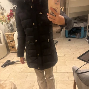 Svart lång pufferjacka Rockandblue - Säljer en svart lång pufferjacka från Rockandblue med stor fluffig huva och dragkedjor vid fickorna. Jackan har quiltad design, tryckknappar och Rockandblue-logga på ärmen. Perfekt för kalla dagar och riktigt snygg passform. Använt fåtal ggr men inga tecken på användning. Skriv för fler bilder. Pris kan diskuteras💕