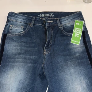 Blå denimjeans med blå sammhetsrand - Snygga blå jeans från Denim med blåa sammetsliknande revärer längs sidorna. Klassisk femficksmodell, normal passform och medelblå tvätt med slitningar framtill. Tillverkade i bomull och jeansmaterial. Perfekta för en trendig vardagslook.