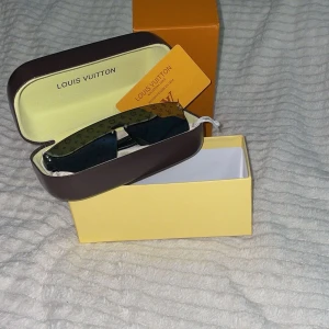 LV svarta monogram solglasögon - Snygga svarta solglasögon från Lvmed rektangulär form och ikoniskt monogrammönster på glasen. Glasögonen har breda skalmar med logotyp och levereras i originaletui och ask. Perfekt accessoar för en trendig look.