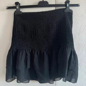 Svart volangkjol med smock - Supersnygg svart, kort kjol från Nelly som är helt oanvänd💖