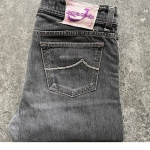 Grå jeans från Jacob Cohën, stl 35 - Snygga grå jeans från Jacob Cohën i klassisk rak modell. Jeansen har kontrastsömmar, femficksdesign och coola detaljer som mönstrat innerfoder. Tillverkade i mjuk bomullsdenim för skön komfort. Perfekta för dig som gillar stilrena och exklusiva jeans. Har ett hål på låret och en påsydd knapp eftermarknad!