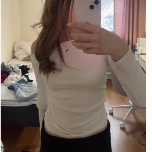 Vit offshoulder långärmad topp - Säljer en stilren vit offshoulder topp med långa ärmar. Toppen har en tight passform. Perfekt för dig som gillar minimalistisk och clean stil. Framhäver axlarna snyggt och passar till många olika outfits.