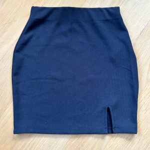 Svart tight kortkjol från New Yorker - Svart, figurnära kortkjol från new yorker i storlek XXS. Kjolen har en liten slits framtill och är gjord i ett stretchigt syntetmaterial. Använd endast en gång så i toppen skick. 