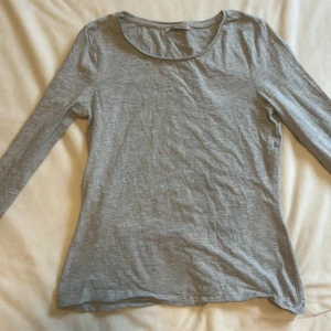 Grå långärmad tröja från Anna field  - En enkel och stilren grå långärmad tröja från Anna  Field. Tröjan har rund halsringning och är tillverkad i ett mjukt och tunt material som känns skönt mot huden. Perfekt att bära som lager eller för en clean look.