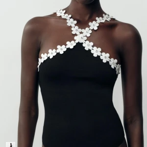 Svart body med vita blommor - Supersnygg svart body med vita blommor som är korsade axelband fram och raka band bak. 