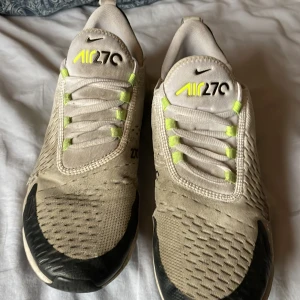 Nike Air 270 sneakers vit/neongul - Nike Air 270 sneakers i vitt med neongula detaljer och svart på tå och häl. Snygg mesh-överdel och synlig Air-enhet i hälen. Skorna har snörning och cool branding på plös och baksida. Perfekt för dig som gillar sportig stil och komfort.