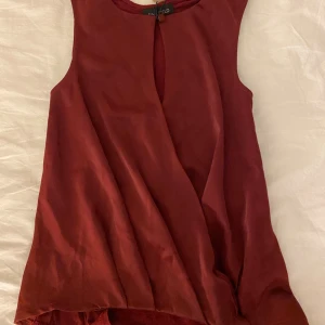Vinröd omlottopp från Anna Field - Säljer en vinröd ärmlös omlottopp från Anna Field. Toppen har en snygg omlottdesign framtill. Materialet är mjukt och har en lätt glansig yta som ger en elegant känsla. Ny med lapp kvar 