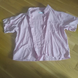 Ljusrosa kortärmad skjorta 157 - Kortärmad skjorta i ljusrosa från 157. Skjortan har klassisk krage, bröstficka och knäppning framtill. Tillverkad i mjuk bomull och har en loose fit som ger en avslappnad vibe.