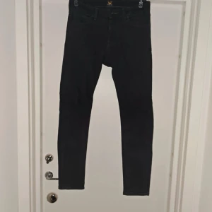 Svarta slim fit jeans Lee Malone W31 L32 - Svarta jeans från Lee, modell Malone, med slim fit och klassisk femficksdesign. Tillverkade i en stretchig mix av bomull, polyester och elastan för en bekväm passform. Perfekta för dig som gillar en smal siluett och stilren look. Skriv om ni har några frågor. 