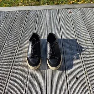 Svarta sneakers från Axel Arigato - Snygga svarta sneakers från Axel Arigato med klassisk låg profil och vit sula. Skorna är i skinn med detaljer i mocka vid tån och har svarta snören. Diskret Arigato-logga i guld på sidan. Perfekta för en stilren och clean look.