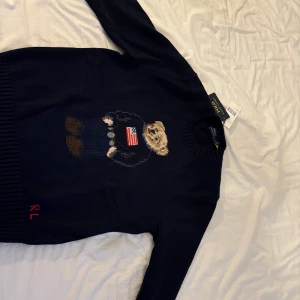Mörkblå stickad tröja Polo Bear - Mörkblå stickad tröja från Polo Ralph Lauren med ikoniska Polo Bear broderad framtill. Tröjan har rund hals, långa ärmar och ribbade muddar. RL-broderi i rött nertill. Perfekt för dig som gillar klassisk och cool stil. Pris kan diskuteras vid snabb affär😁