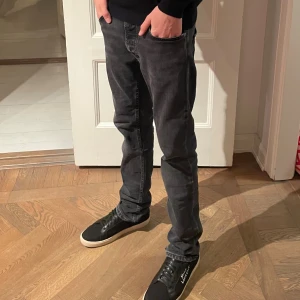  Nudie Jeans - Säljer ett par svarta jeans från Nudie Jeans med klassisk femficksdesign och diskret vågmönster på bakfickorna. Jeansen har rak passform och är tillverkade i mjukt denimtyg. Perfekta för dig som gillar en stilren och enkel look. Storlek 29/32 modell grim tim . Ny pris 1599