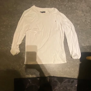 Vit långärmad tröja Tommy Hilfiger - Vit långärmad tröja från Tommy Hilfiger med en liten broderad logga på bröstet. Klassisk och enkel design med rund halsringning, perfekt till jeans eller kjol. Mjuk och skön bomullskvalitet.