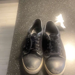 Lanvins  - Svarta sneakers med klassisk design och vit platt sula. Skorna har rund tå, snörning och är tillverkade i skinnliknande material. Perfekta för en avslappnad och stilren look.