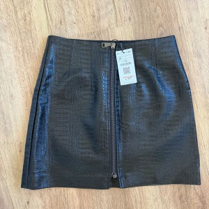 Svart kort kjol i skinnimitation Stradivarius - Svart kort kjol från Stradivarius i skinnimitation med croco-mönster och en snygg dragkedja framtill. 