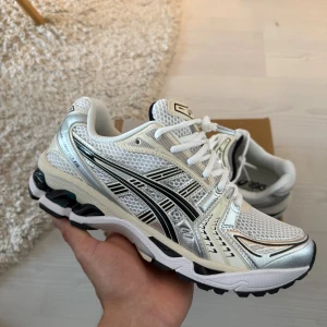  Asics GEL KAYANO 14 white midnight - Säljer ett par Asics GEL sneakers i vitt och silver med svarta detaljer. Skorna har mesh-ovandel för bra andning, snygga silvriga paneler och klassisk snörning. Sulan är robust och designad för bra grepp. Perfekta för dig som gillar sportig och trendig stil. Storlek 43,5. HELT NYA