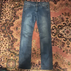 Blå Replay jeans slim fit 32/34 - Snygga blå jeans från Replay med klassisk femficksdesign och raka ben. Jeansen har en diskret tvättad look och Replay-logga på myntfickan. Perfekta för dig som gillar en enkel och stilren stil. Materialet är mjukt jeans-tyg som sitter skönt hela dagen. Midja 40cm längd 105cm (43)