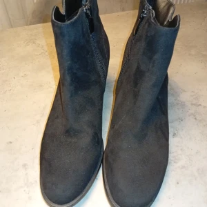 Svarta mocka-look stövletter med klack - Snygga svarta stövletter i mocka-look med dragkedja på sidan och stabil klack. Skorna har en rund tå och en stilren design som passar perfekt till jeans eller klänning. Klacken är medelhög och ger en schysst siluett.