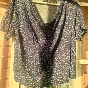 Blommig blå topp från Lindex - Snygg topp från Lindex med småblommigt mönster i ljusblått. Modellen har korta ärmar och en lös passform med lätt draperad halsringning. Tillverkad i 100% mjuk viskos som känns skön mot huden.