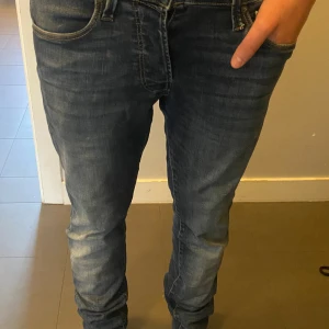 Jack and Jones  - Snygga blå jeans från Jack and Jones ,  med tapered passform. Jeansen har klassisk femficksdesign, dragkedja och knapp i midjan. Materialet är mjukt jeans med lätt tvättad look och diskreta slitningar. Perfekt för dig som gillar stilrena och bekväma jeans.