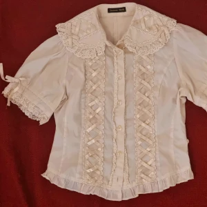 Innocent World lolitablus - Cross Ribbon Round Collar Blouse av Innocent world i Ivory. 450 kr + Frakt eller upphämtning i gbg  Mycket fin märkeslolitablus från 2006. Saknar waist ties och long sleeves. En söm har spruckit i ryggen men inga hål. Elastiken i ärmarna är lite trött.