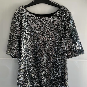 Paljett topp - Snygg festtopp från H&M med silvriga/svarta paljetter i mycket bra skick! Jättesnygg att styla med kort kjol och höga stövlar!