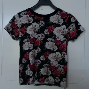 En blomning och somrig T-shirt i ett väldigt bra skick. Mörk och ljusrosa blommer på en mörkblå bas. Använts få gånger. 
