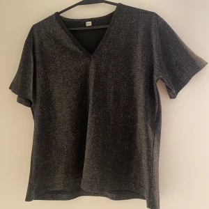 Glittrig topp - Glittrig t-shirt topp, som inte glittrar av sig. V ringad krage, lite pösigare modell. Bara att fråga för bättre bilder.