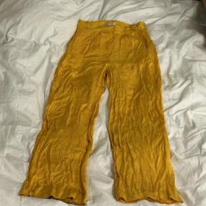 Gula byxor  - Gula svala byxor i lite 90tals stil, bara använda en gång. Spänne och dragkedja på sidan. Det är tunt o ganska glansigt tyg som typ har blommor inbeordrade i tyget(tror jag, se på tredje bilden)