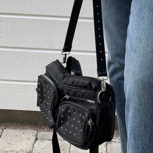Väska - Svart väska med fickor och nitar. Kommer med två band, ett längre och ett kortare med nitar.