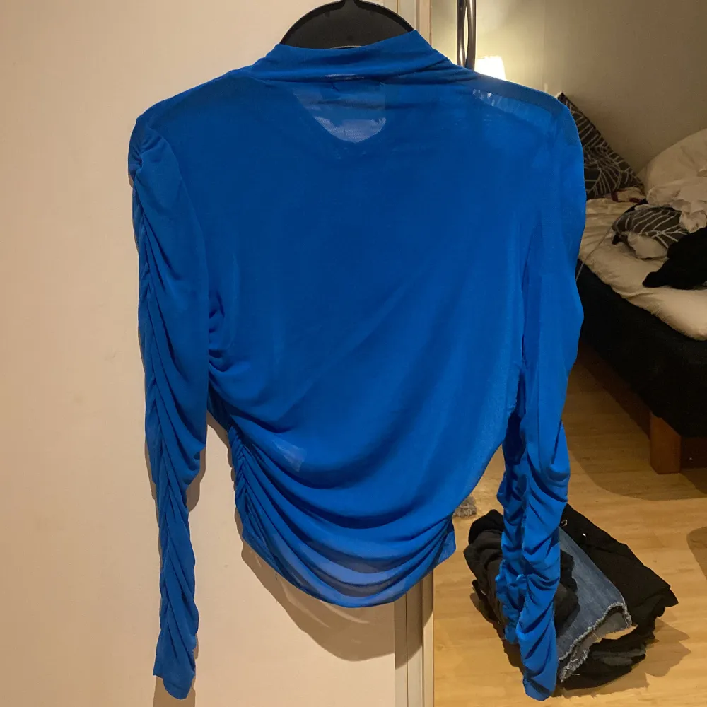 Rynkad, blå tröja från Boohoo typ i mesh. Framsidan är i dubbelt tyg, ryggen och ärmarna i enkelt så de är väldigt genomskinliga. Står strl 40, upplever den som en S eller M då den är stretchig.. Toppar.