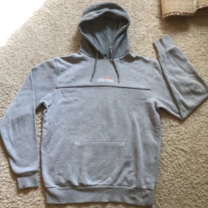En grå Ellesse hodie i storlek M - Grå hoddie i gått skick utan dragkedja men ficka på magen.
