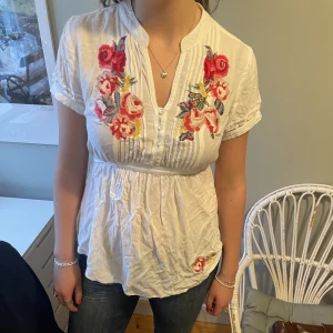 Vit blus - Vit blus med broderade blommor och knytning i ryggen. I mycket gott skick!