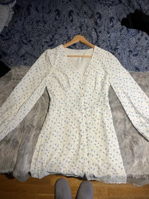 Blommig klänning - Långärmad klänning med knappar framtill. Säljer då den endast har kommit till användning en gång, passar super till midsommar😉💕