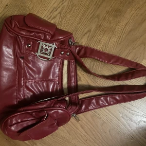 Röd väska - SKITSNYGG väska! Har en liten defekt, ett svart märke (se framsida) men inget som syns supertydligt. Obs notera måtten, den är lite mindre, som en baguettebag❤️ Dragkedjan till framfack fungerar ej, tips sätt ihop m säkerhetsnål då resten av facken funkar