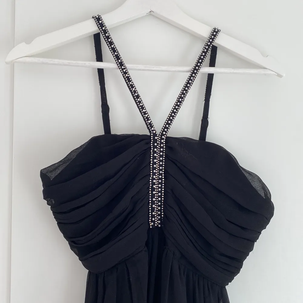Såå vacker svart golvlång balklänning med vita stenar och pärlor på banden och bysten😍 använd en gång och är i jättebra skick💓 storlek 34 från Nelly🖤säljer då den inte kommer till användning💌. Klänningar.