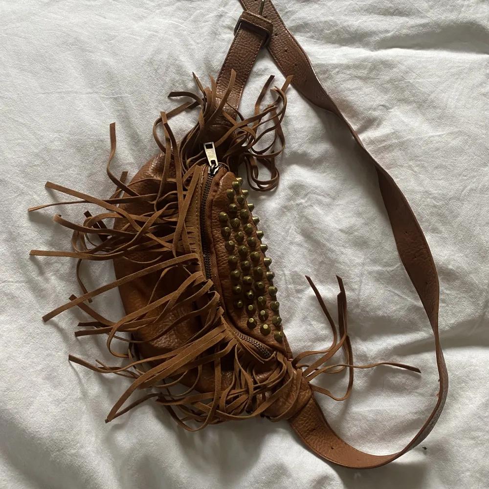 En bumbag ifrån ginatricot i läderimitation och guld detaljer med fransar . Väskor.