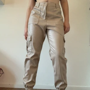 Beige cargopants - Coola beige cargopants i skinn (ej äkta). Storlek M. Midjemått: 73cm Innerbenslängd: 71cm 