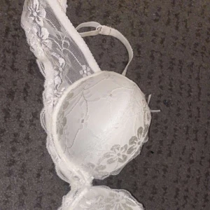 Vit spets bh  - Denna bh är använd en gång och är som i ett nyttskick. Den har fin spets runt om med ett jätte fint blommigt mönster och har en rosett mellan bysten och två rosetter längst upp innan banden börjar. 