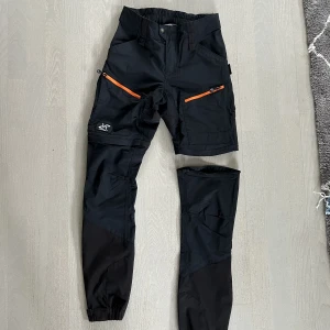 Friluftsbyxor  - Silence zip off pants från Revolution Race i storlek 38/M. Man kan ta bort byxbenen med dragkedja och enkelt göra om dem till shorts. Längst ner finns även små hakar som gör att man kan fästa byxslutet på kängorna. Något tajta kring låren för storleken. 