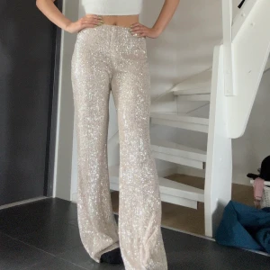 Glittriga byxor - Glittriga byxor från NA-KD i  en fin champagne beige färg. Eftersom det är individuella paljetter som är fastsydda så finns det småtrådar som är lösa på vissa ställen MEN det är absolut inget som syns när man har på sig dom.