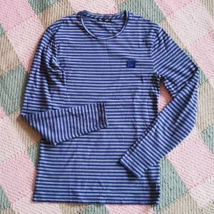 Långärmad T-shirt - Acne Studios - Blå- och grårandig långärmad T-shirt i unisex-modell från ACNE Studios. Storlek XS, funkar för kvinna i storlek S. Modellen heter NAPA L FACE från höst/vinter 2017. 100% bomull, ingen stretch. Bra skick, men använd flera qgånger. Axelbredd 41 cm, längd 66