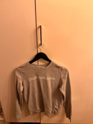Grå tröja, Calvin Klein - Grå långärmad tröja från Calvin Klein Jeans. Sparsamt använd så i väldigt fint skick