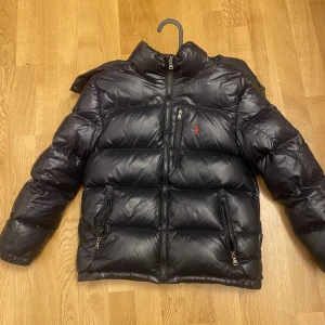  Polo Ralph Lauren  jacka  - Hej jag säljer min polo Ralph Lauren vinter jacka nu för den har blivit för liten köpt för 2200kr för 2 år sedan den är varm på vintern säljer billigare för en ficka har fastnat på den men det går säkert att trassla ut om man vill den är svart glansig 