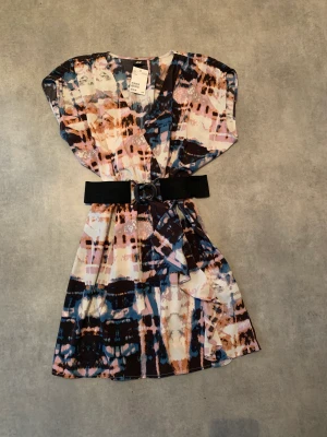 Ny H&M klänning strl.38 - Snygg klänning från H&M i storlek 38. Skärpet är i stretch och sitter i två öglor i midjan, men det går att ta bort om man vill. I kjolen är det som omlott. 100% polyester, tvättas i 40 grader. Hann aldrig använda denna innan graviditeten.