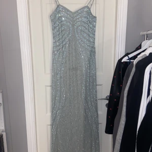 Glittrig maxiklänning  - Grön/grå/blå maxiklänning med lappen kvar. Nypris 1445. Litet hål i yttersta tyget vid dragkedjan men inget som påverkar dess funktion (därav priset)😊