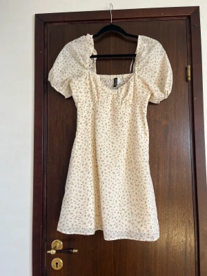 Blommig klänning - Säljer denna beige blommiga klänningen då den aldrig använts, den har fortfarande lappar kvar. På bilden ser den beigare än vad den egentligen är utan den är mer ljusbeige