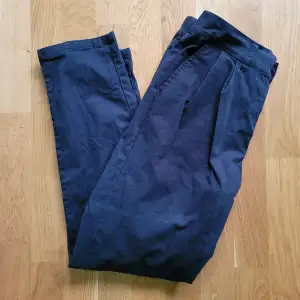 Mörkblå byxor i grovt tyg med fickor, stretch i midjan och knappgylf. Byxorna har varit insydda och det är märken efter på tre ställen. Exempel på sista bilden.